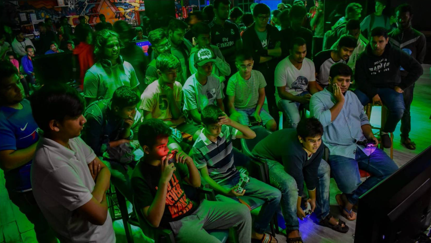 A group of boys seated in front of a TV. Two hold video game remotes.