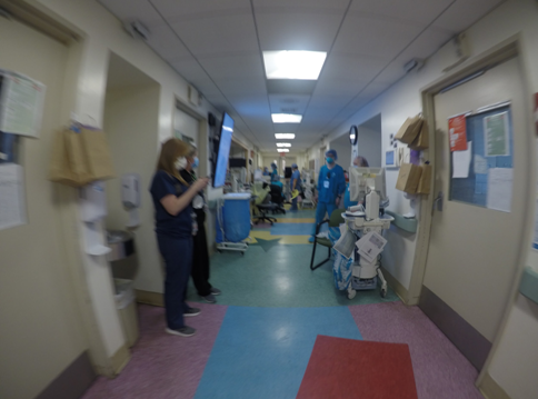 The hallway of a hospital, with a few people wearing medical scrubs and facemasks.
