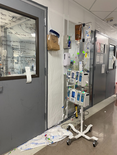 A mobile cart with IV bags and machines in a hospital hallway.