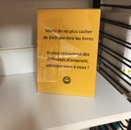 A sign in the library asking patrons not to hide the DVDs, with a smiley face at the bottom.
