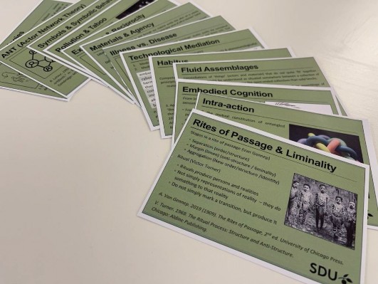 Green cards with white borders and printed text featuring theories and illustrations, as well as a university logo. The cards are splayed out in an arc on a table.
