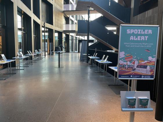 Hallway with “Spoiler Alert” sign at the forefront and student projects on tables lining either side of walkway.