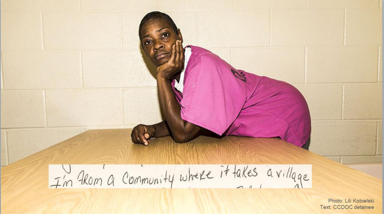 Female detainee at Cook County Jail in pink scrubs leaning on a table. Handwritten text by a female detainee reads, “I'm from a community where it takes a village.”