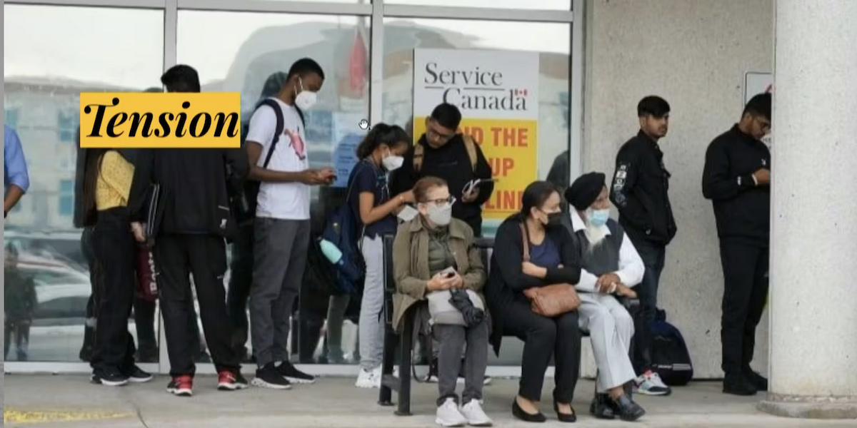 photograph of a diverse group of people waiting outside a building with a "Service Canada sign", most are wearing masks.